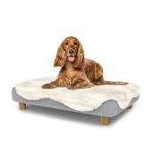 Perro sentado en una cama para perros mediana Topology con topper de piel de oveja y patas redondas de madera