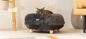 Gato tumbado en una cama para gatos de color gris con patas de madera de diseño.