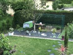 Un jardín con un gran gallinero verde Cube y un corral anexo