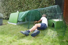 Una persona demostrando cómo se limpia un corral de conejos conectado a una conejera verde