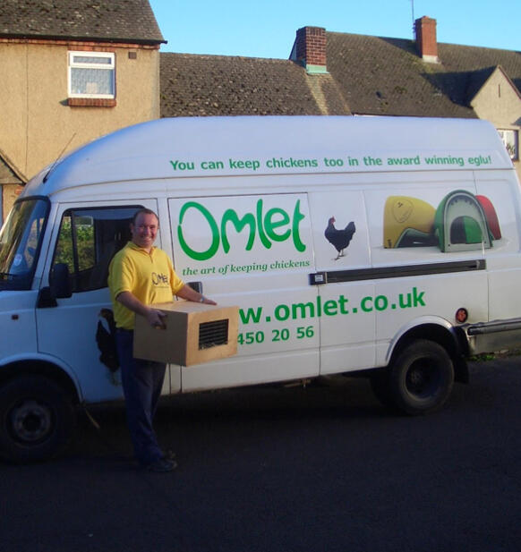 Un repartidor junto a una furGoneta de la marca Omlet que transporta una caja de pollos