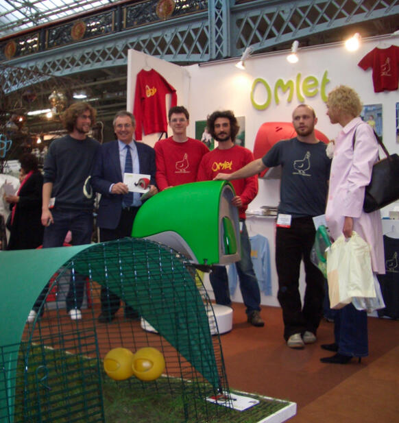 Un grupo de personas posa en un stand con el gallinero Eglu Cube 