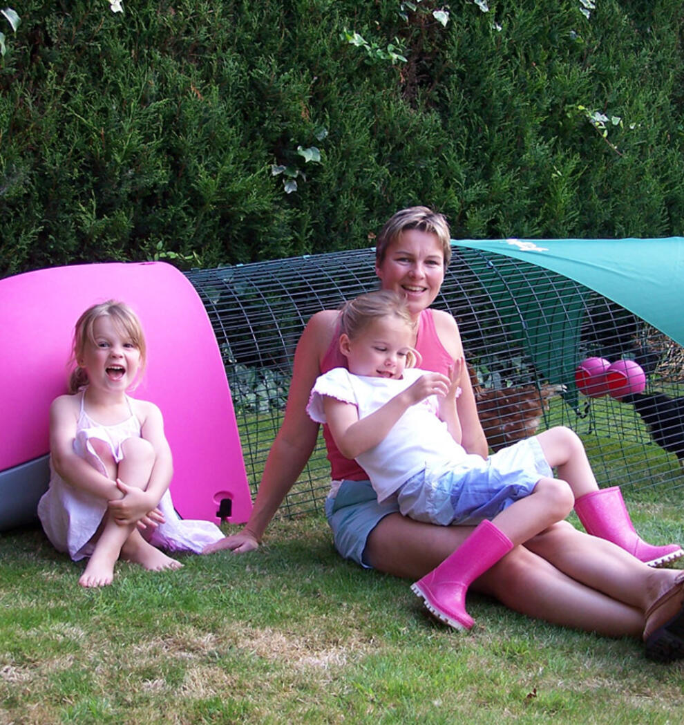 Una familia sentada junto a un gallinero rosa Eglu 