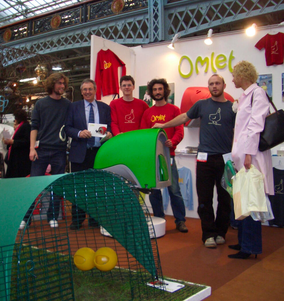 Un grupo de personas posa en un stand con el gallinero Eglu Cube 
