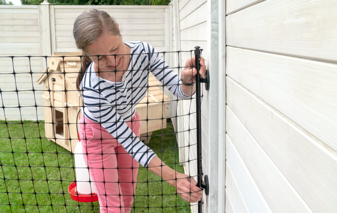 Mujer fijando la valla para gallinas de Omlet a un muro de madera en el jardín