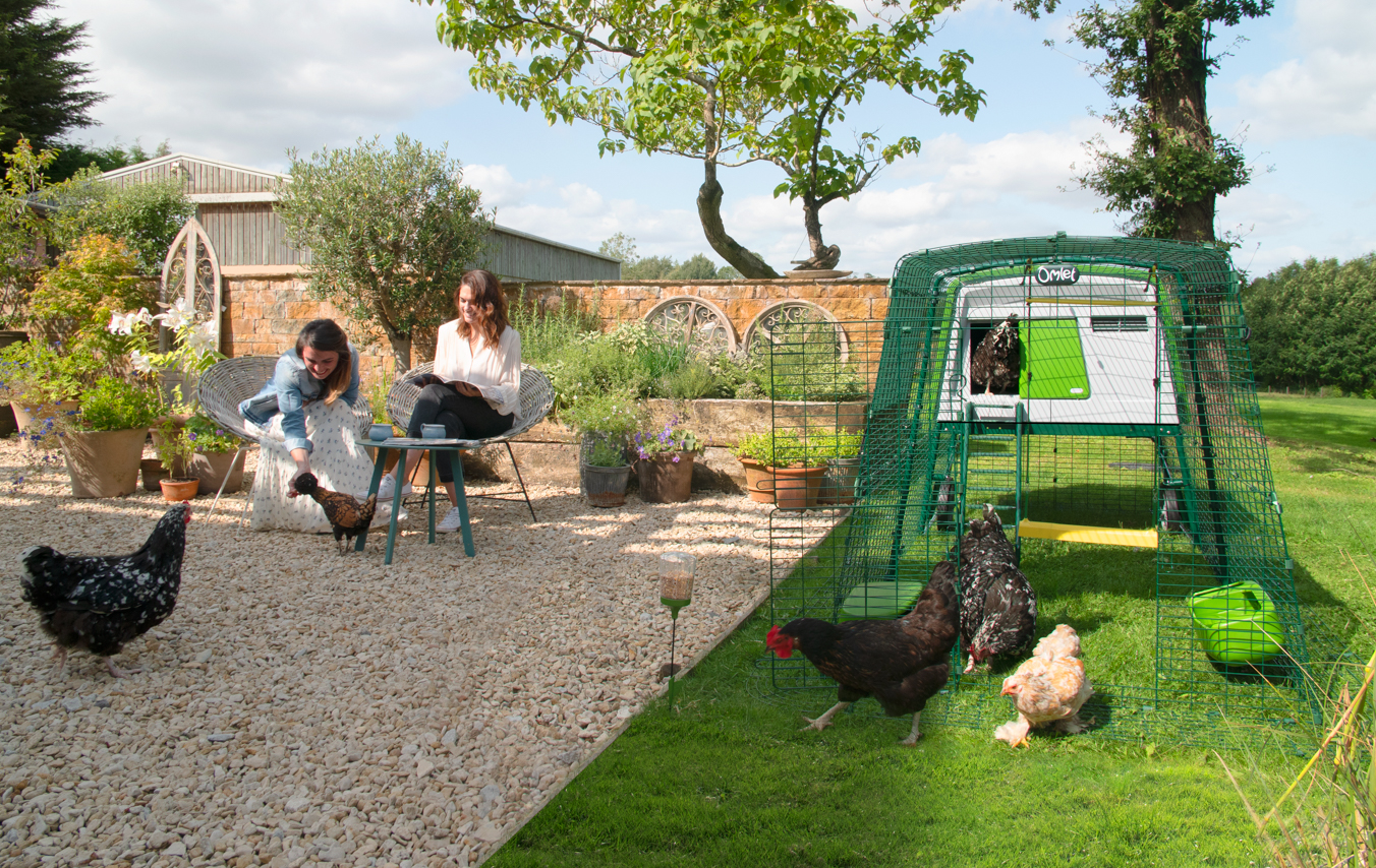 dos mujeres comiendo en el jardín y gallinas libres alrededor de su gallinero eglu Cube