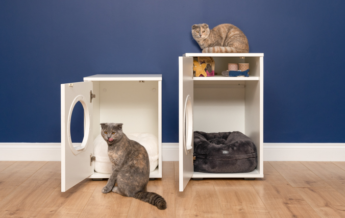 Dos gatos junto a las modernas casas de interior para gatos. Podemos ver su interior, una de ellas tiene espacio de almacenamiento.